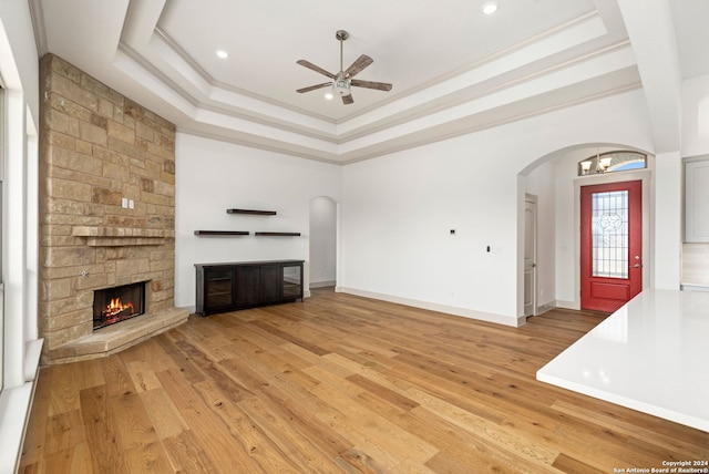 unfurnished living room featuring light wood-type flooring, ceiling fan, a fireplace, a tray ceiling, and crown molding