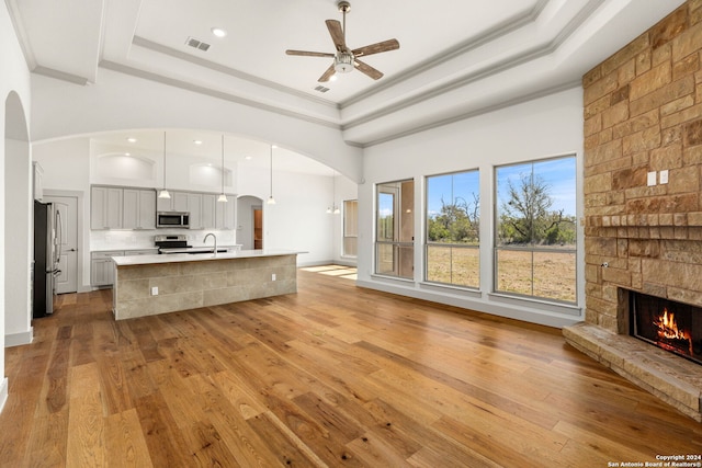 kitchen featuring light hardwood / wood-style floors, a tray ceiling, a center island with sink, hanging light fixtures, and appliances with stainless steel finishes