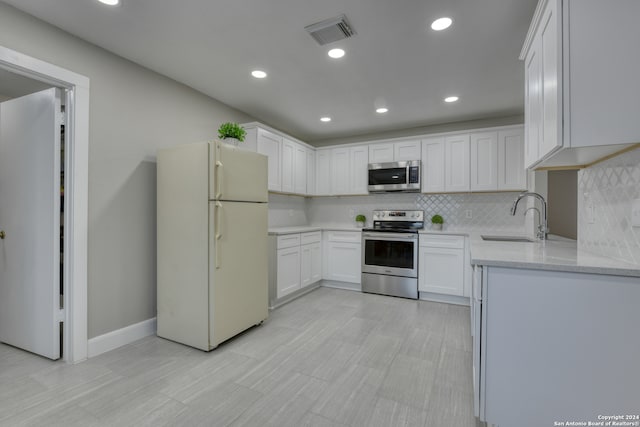 kitchen with light stone counters, decorative backsplash, stainless steel appliances, white cabinets, and sink