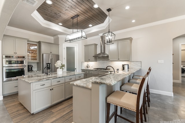 kitchen with a breakfast bar, kitchen peninsula, wall chimney range hood, appliances with stainless steel finishes, and decorative light fixtures