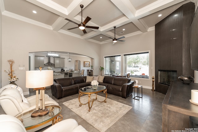 living room featuring ceiling fan, a fireplace, crown molding, and beam ceiling