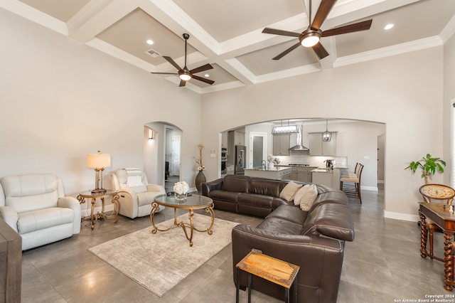 living room with beamed ceiling, ceiling fan, a high ceiling, crown molding, and coffered ceiling