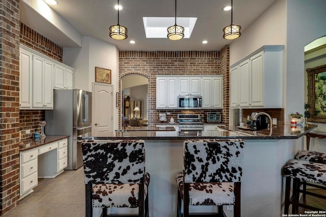 kitchen with pendant lighting, brick wall, stainless steel appliances, kitchen peninsula, and a kitchen bar