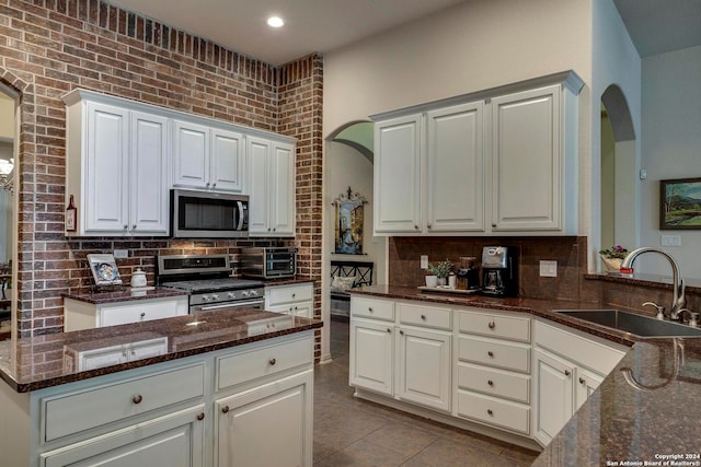 kitchen featuring appliances with stainless steel finishes, sink, dark stone counters, and white cabinetry