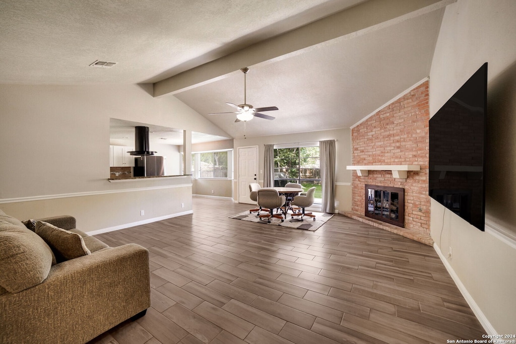 living room with ceiling fan, a textured ceiling, lofted ceiling with beams, a fireplace, and dark hardwood / wood-style flooring