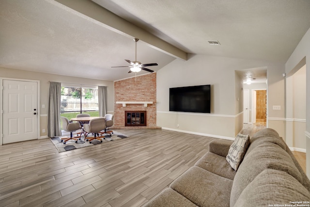 living room featuring ceiling fan, a brick fireplace, a textured ceiling, lofted ceiling with beams, and light hardwood / wood-style floors