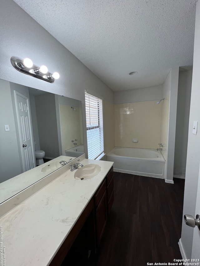 bathroom featuring a bathtub, toilet, wood-type flooring, vanity, and a textured ceiling