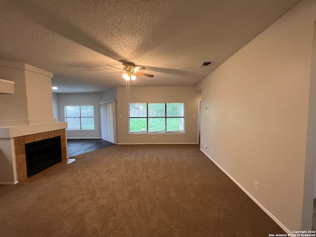 unfurnished living room with ceiling fan, a textured ceiling, a fireplace, and dark carpet