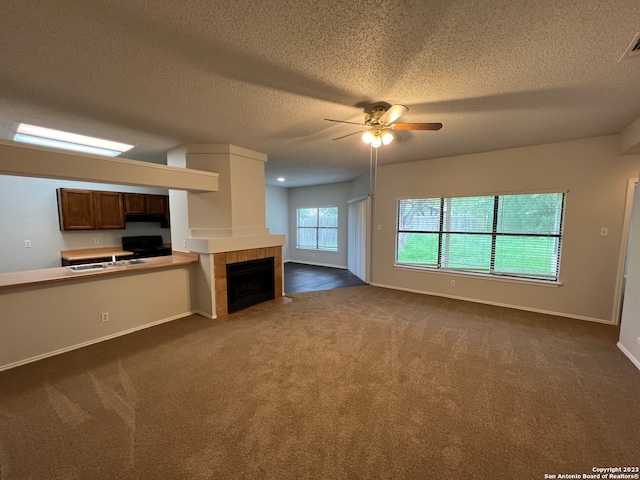 unfurnished living room with ceiling fan, dark carpet, sink, a fireplace, and a textured ceiling