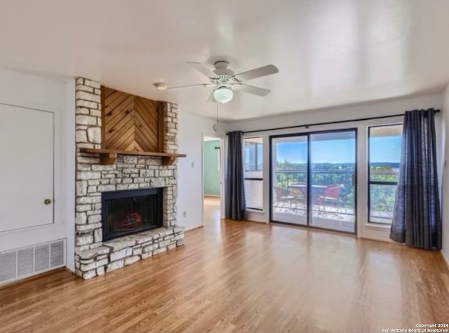 unfurnished living room featuring hardwood / wood-style flooring, ceiling fan, and a stone fireplace