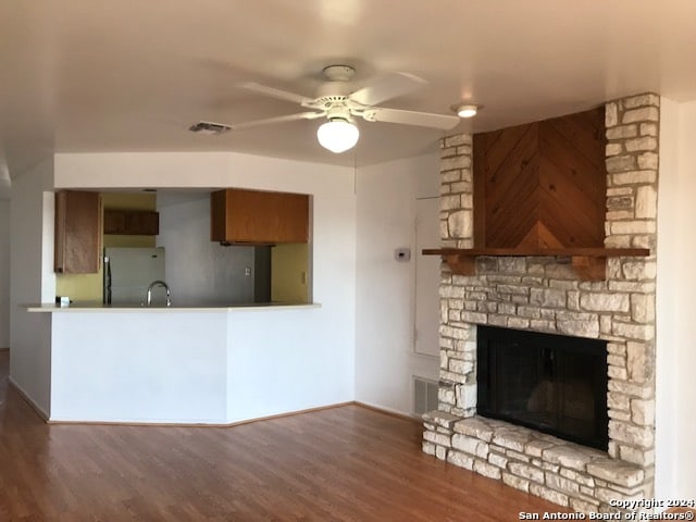 unfurnished living room featuring ceiling fan, a stone fireplace, sink, and wood-type flooring