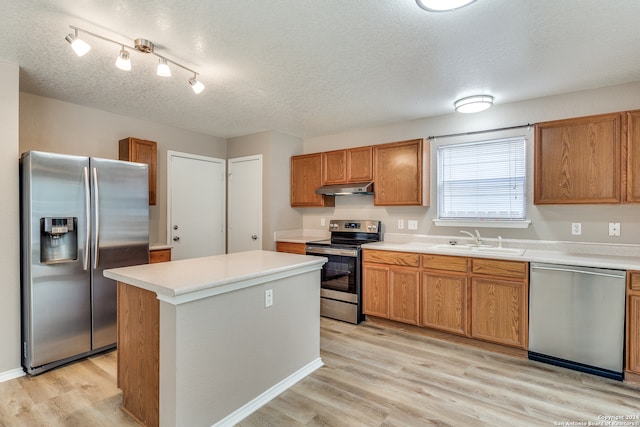 kitchen with sink, a kitchen island, a textured ceiling, light hardwood / wood-style flooring, and appliances with stainless steel finishes