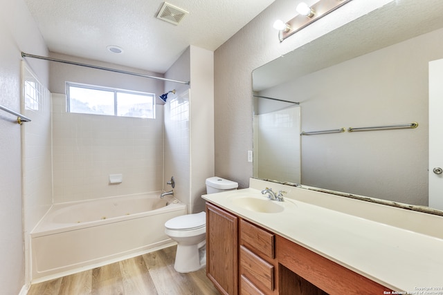 full bathroom featuring toilet, wood-type flooring, tiled shower / bath combo, vanity, and a textured ceiling