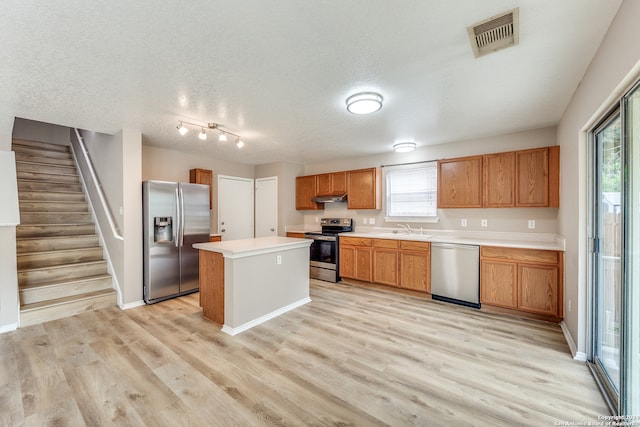 kitchen with a center island, stainless steel appliances, sink, light hardwood / wood-style floors, and a textured ceiling