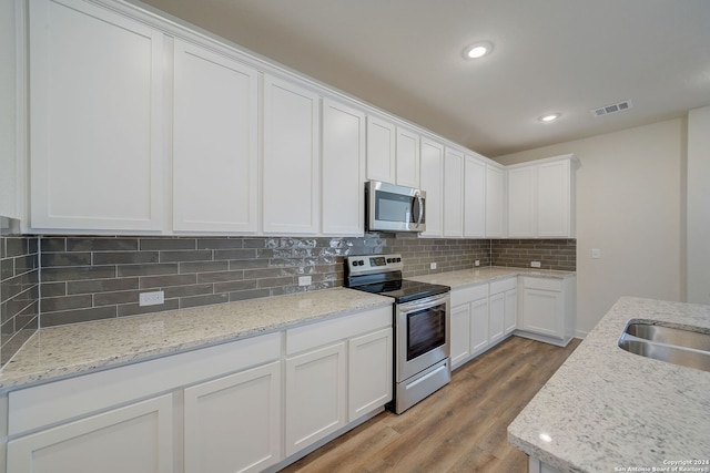 kitchen with white cabinets, light stone countertops, appliances with stainless steel finishes, light wood-type flooring, and decorative backsplash