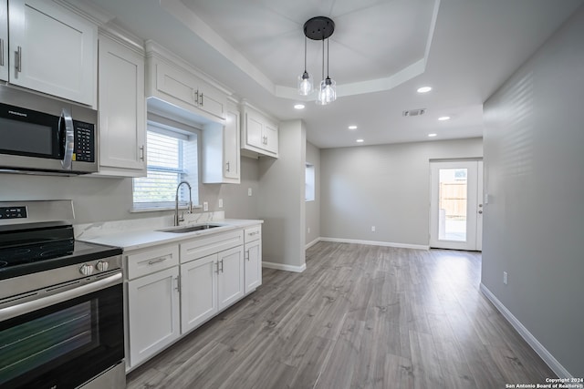 kitchen featuring sink, decorative light fixtures, white cabinetry, appliances with stainless steel finishes, and light wood-type flooring