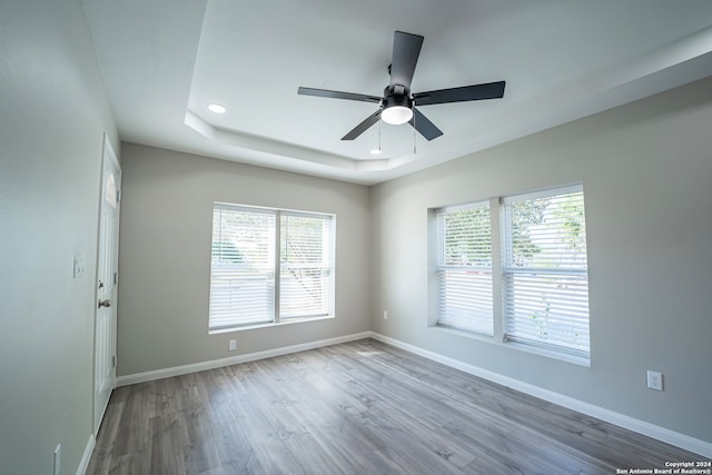 unfurnished room featuring hardwood / wood-style flooring, a healthy amount of sunlight, ceiling fan, and a raised ceiling