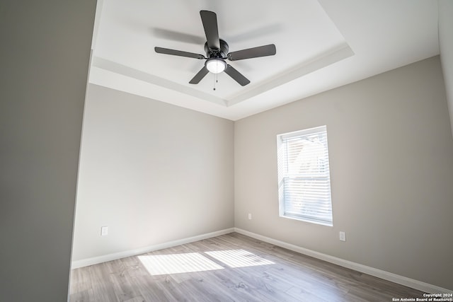 empty room featuring a raised ceiling, light hardwood / wood-style floors, and ceiling fan