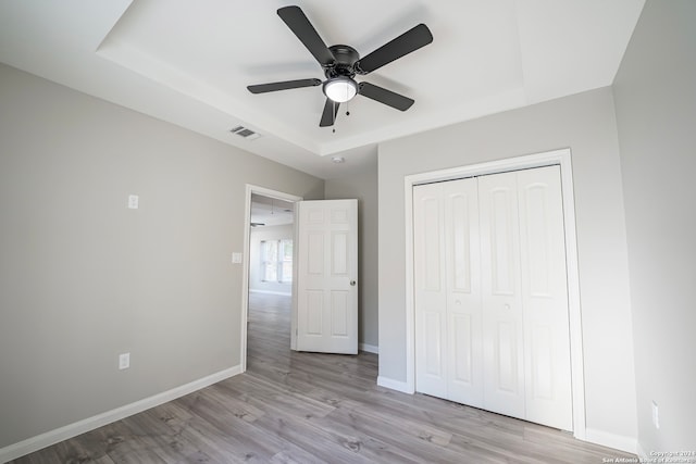 unfurnished bedroom with ceiling fan, a closet, a raised ceiling, and light hardwood / wood-style flooring