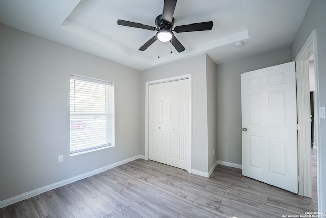 unfurnished bedroom with a closet, a tray ceiling, light wood-type flooring, and ceiling fan