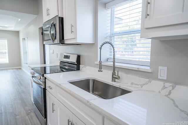 kitchen featuring light hardwood / wood-style flooring, sink, light stone counters, white cabinets, and appliances with stainless steel finishes