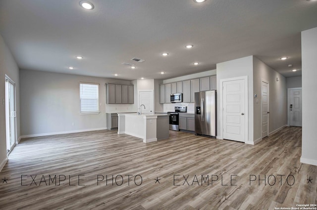 kitchen featuring a kitchen island with sink, gray cabinetry, sink, light hardwood / wood-style flooring, and appliances with stainless steel finishes