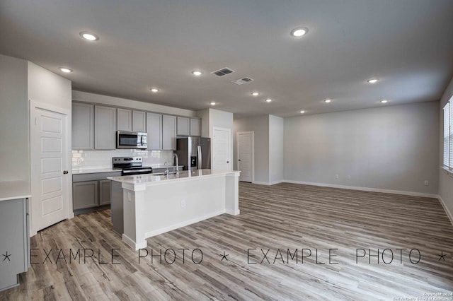 kitchen featuring appliances with stainless steel finishes, gray cabinetry, a center island with sink, and light hardwood / wood-style floors