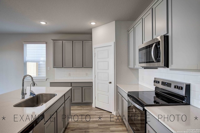 kitchen featuring gray cabinets, light hardwood / wood-style flooring, sink, backsplash, and appliances with stainless steel finishes