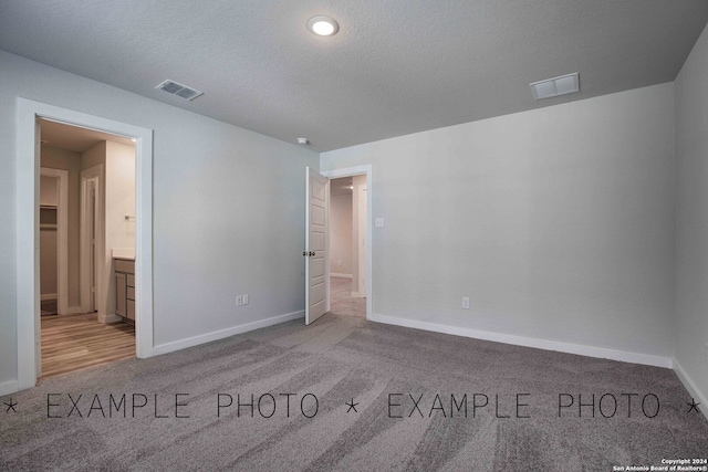 unfurnished bedroom featuring light colored carpet, a textured ceiling, and ensuite bathroom