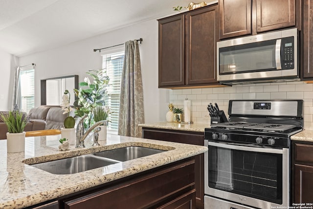 kitchen with light stone counters, dark brown cabinetry, sink, appliances with stainless steel finishes, and backsplash