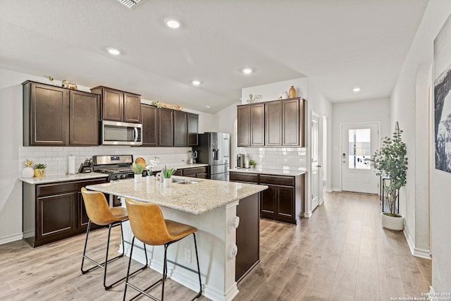 kitchen featuring tasteful backsplash, a center island with sink, appliances with stainless steel finishes, a kitchen breakfast bar, and light wood-type flooring