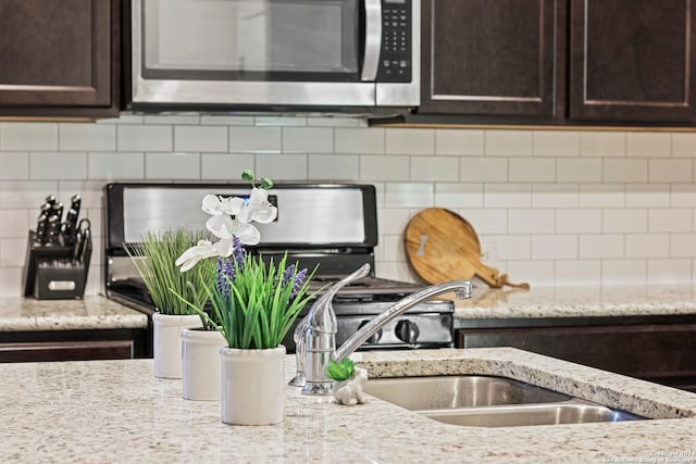 kitchen featuring dark brown cabinets, backsplash, sink, and light stone counters