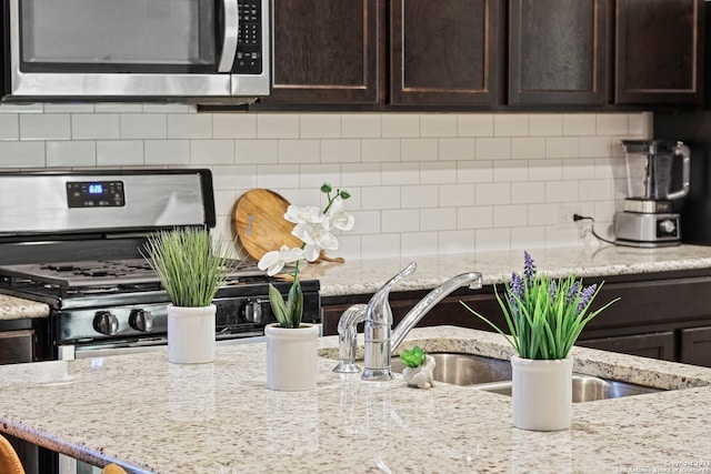 kitchen featuring dark brown cabinets, light stone counters, stainless steel appliances, and backsplash