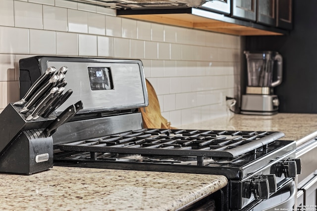 kitchen with light stone countertops, backsplash, and stainless steel range with gas stovetop