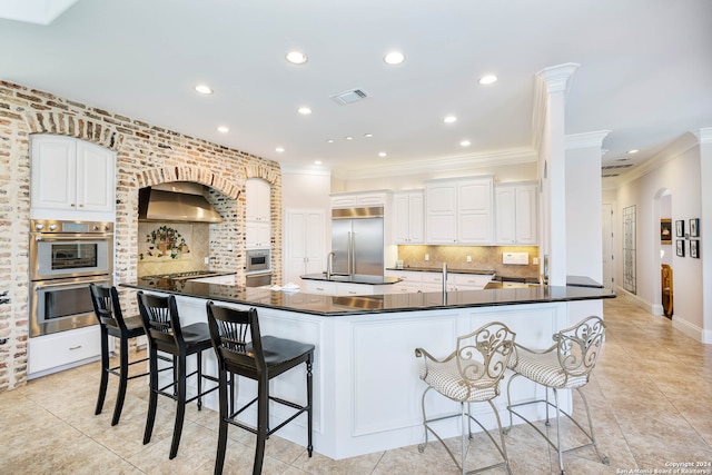 kitchen with decorative backsplash, white cabinets, built in appliances, and range hood