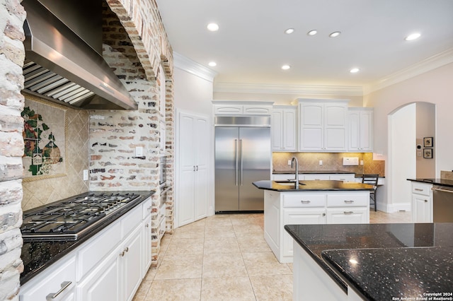 kitchen with decorative backsplash, stainless steel appliances, white cabinets, wall chimney exhaust hood, and dark stone counters