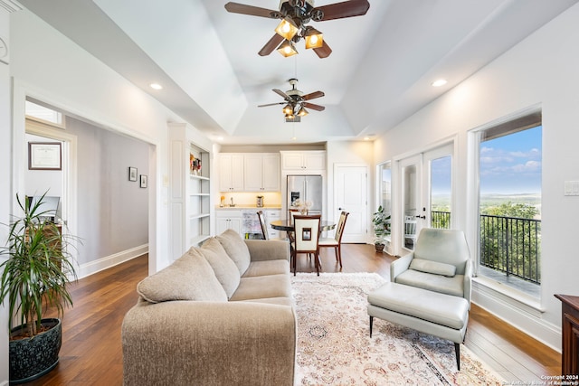 living room with a tray ceiling, ceiling fan, dark wood-type flooring, and vaulted ceiling