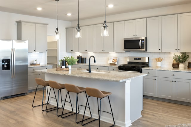 kitchen featuring light wood-type flooring, stainless steel appliances, sink, hanging light fixtures, and an island with sink