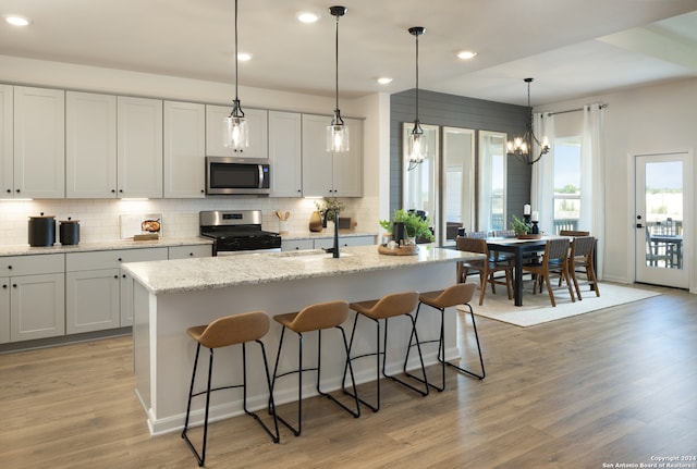 kitchen featuring stainless steel appliances, a kitchen island with sink, sink, pendant lighting, and light hardwood / wood-style flooring