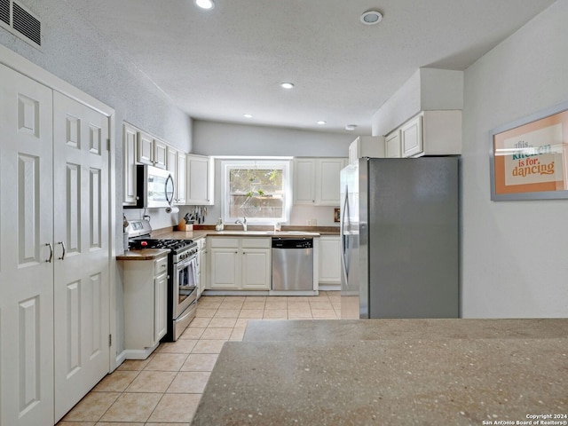 kitchen with lofted ceiling, appliances with stainless steel finishes, light tile patterned floors, and white cabinetry