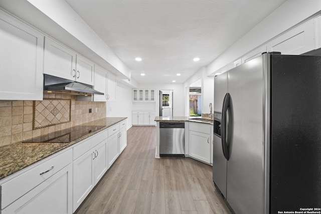 kitchen with dark stone countertops, light wood-type flooring, white cabinets, stainless steel appliances, and backsplash