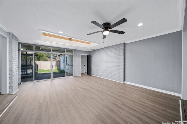 interior space with a skylight, a textured ceiling, ornamental molding, brick wall, and hardwood / wood-style floors