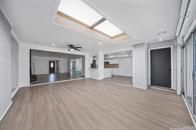 unfurnished living room with ceiling fan, brick wall, a skylight, and light hardwood / wood-style floors