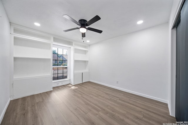 unfurnished living room with hardwood / wood-style flooring, built in shelves, and ceiling fan