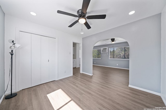 unfurnished bedroom with ceiling fan, a wall unit AC, hardwood / wood-style floors, and a closet