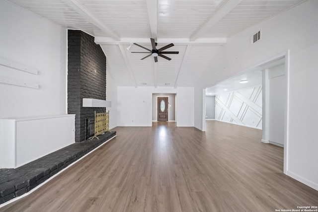 unfurnished living room featuring a brick fireplace, beam ceiling, wood-type flooring, and ceiling fan