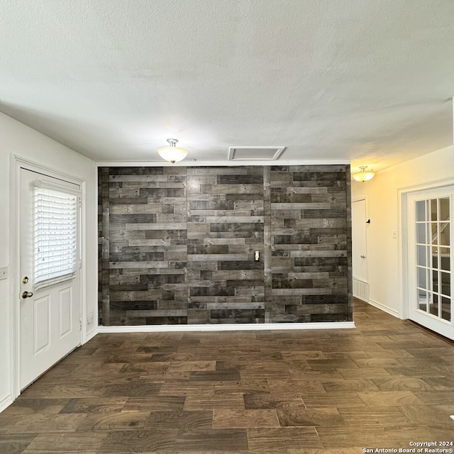 empty room featuring a textured ceiling, wood walls, and dark hardwood / wood-style floors