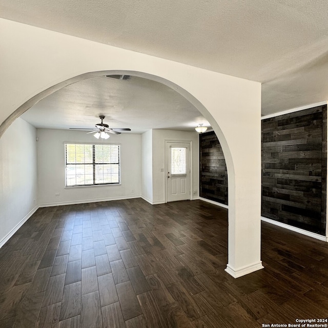 interior space featuring wooden walls, ceiling fan, dark wood-type flooring, and a textured ceiling