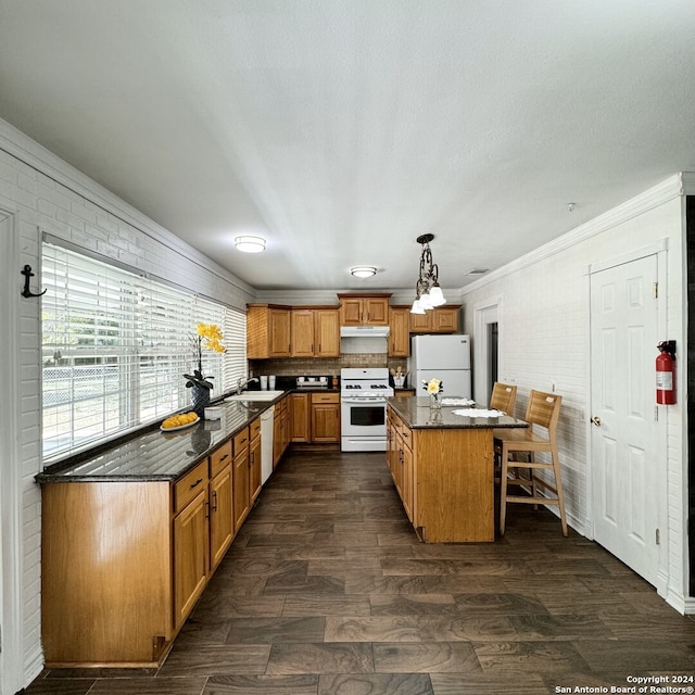 kitchen with dark hardwood / wood-style floors, white appliances, sink, brick wall, and pendant lighting