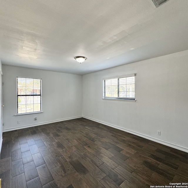 spare room with a textured ceiling, plenty of natural light, and dark wood-type flooring